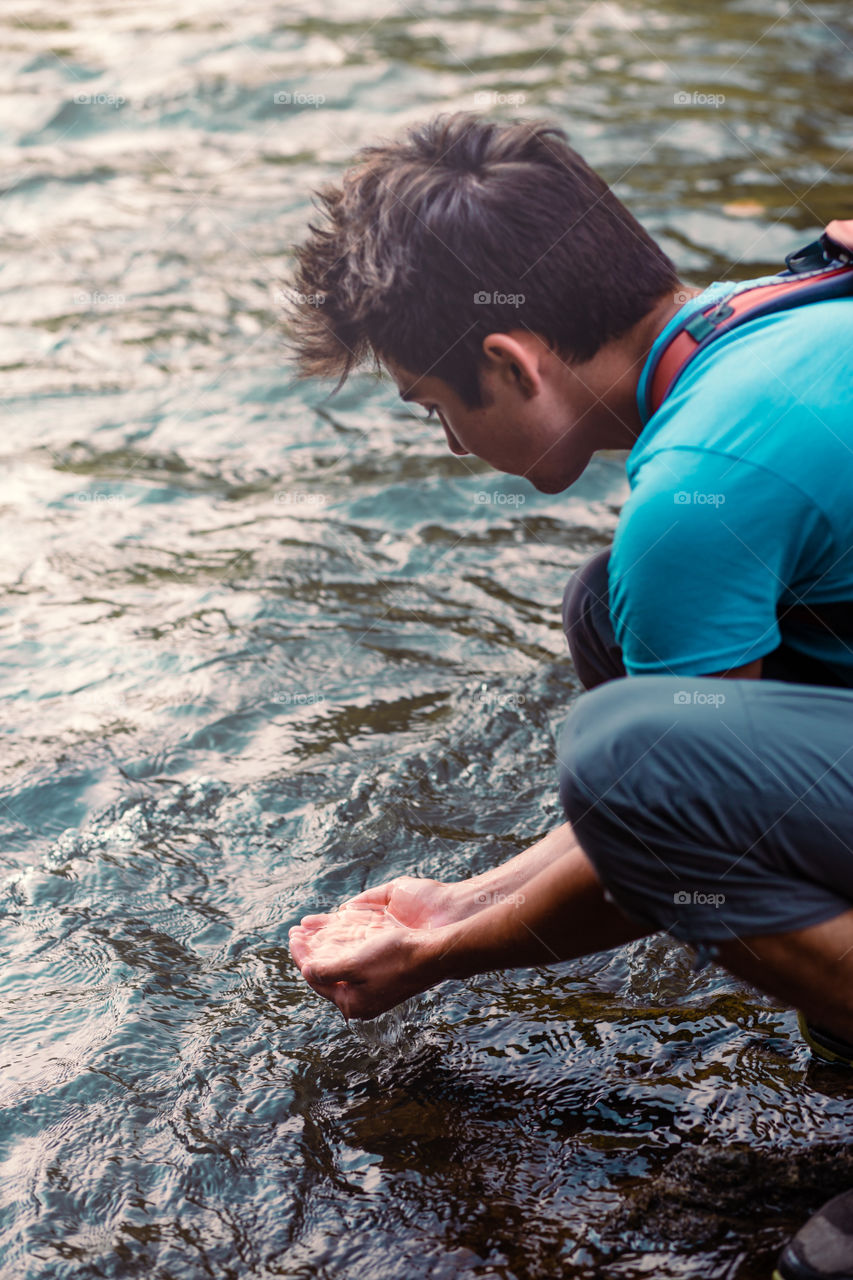 Young boy taking pure water from a river and holding it in the hands