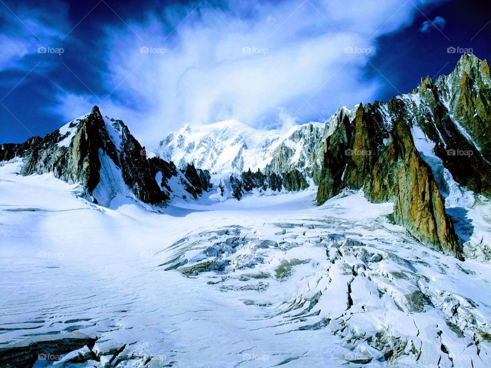 Spectacular view of the Mer de Glace glacier with jagged mountains in the background and bright blue sky with cloud formations