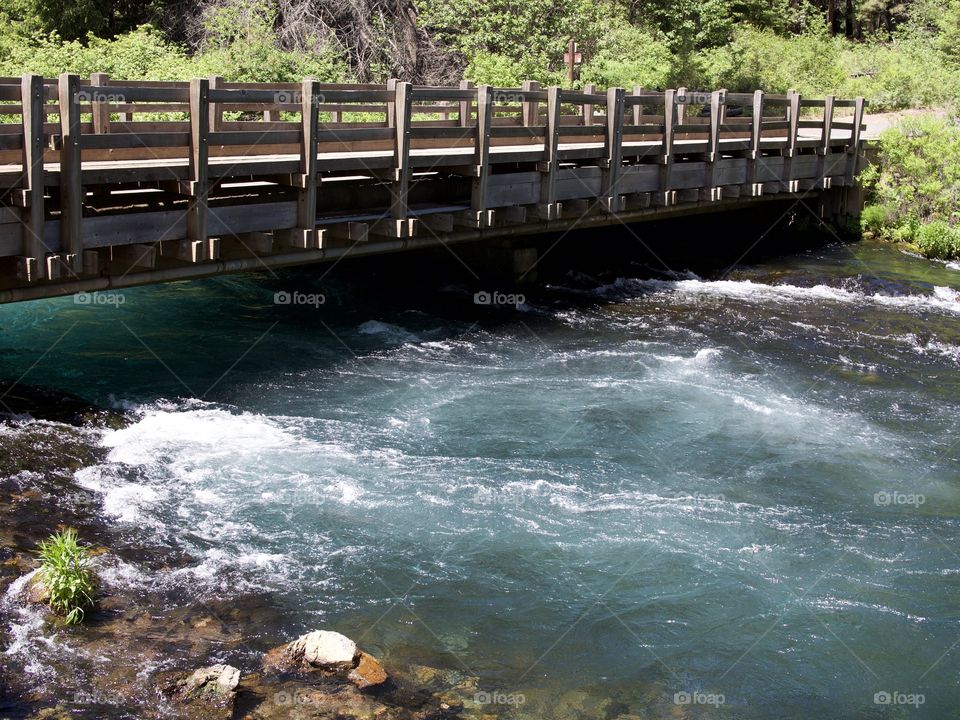 A bridge crossing over the absolutely stunning turquoise waters of Wizard Falls in the Metolius River on a sunny summer morning in Central Oregon. 