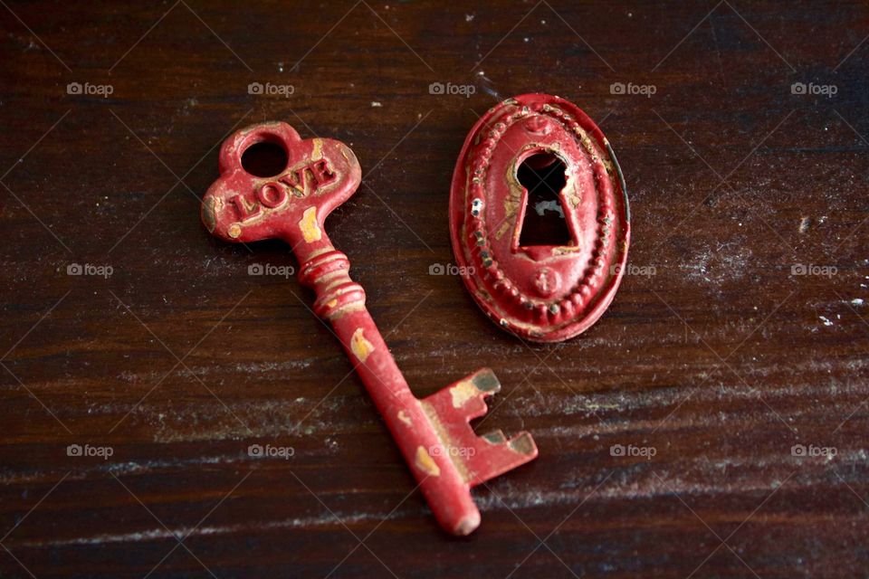 Red rustic vintage key with the word “LOVE” and keyhole on dark wooden surface