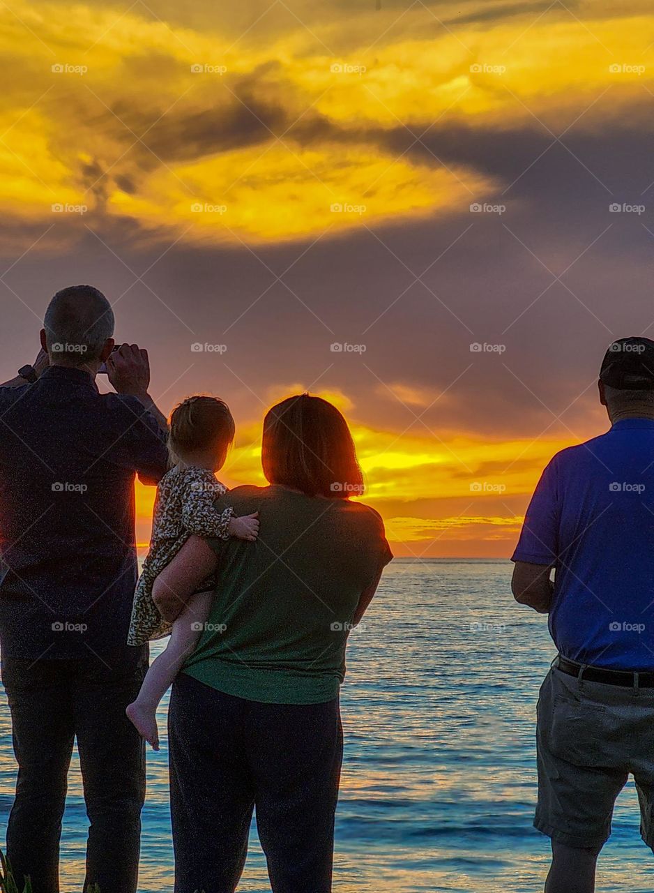 A family takes in a beautiful sunset looking out over the Pacific Ocean from San Diego California