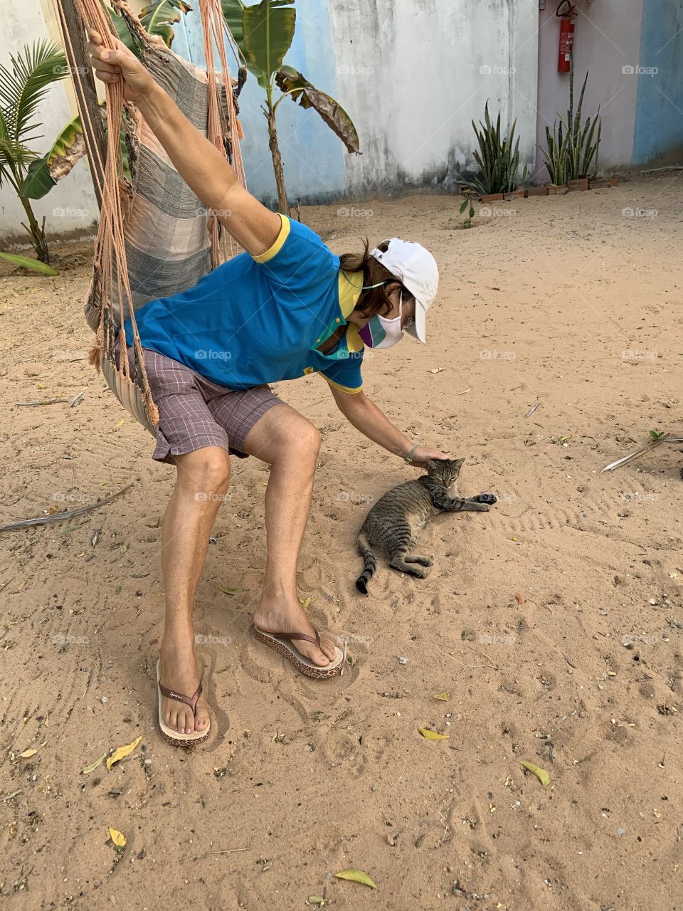 Woman sitting in the hammock with mask cuddling cat