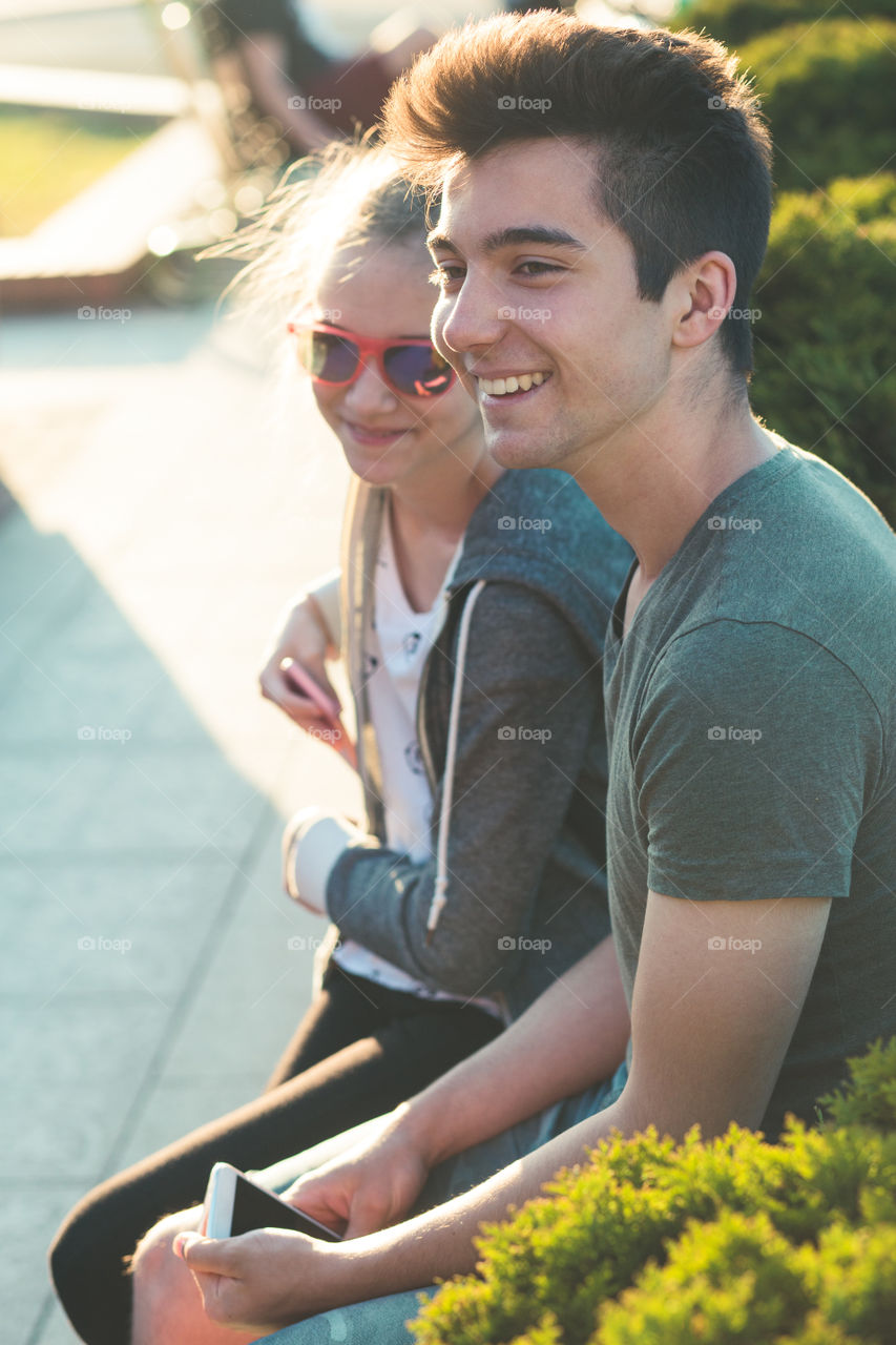 Couple of friends, teenage girl and boy,  having fun together, sitting in center of town, spending time together