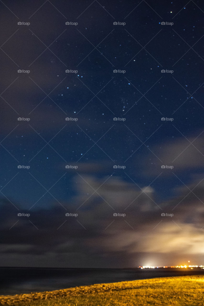 Magical evening along the beach. Stars, clouds, city lights, waves and sand make this night landscape magical.