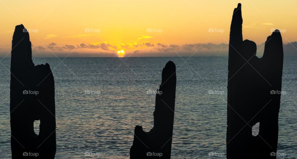 The sun rising above the English Channel, throwing the old sea defences into silhouette 