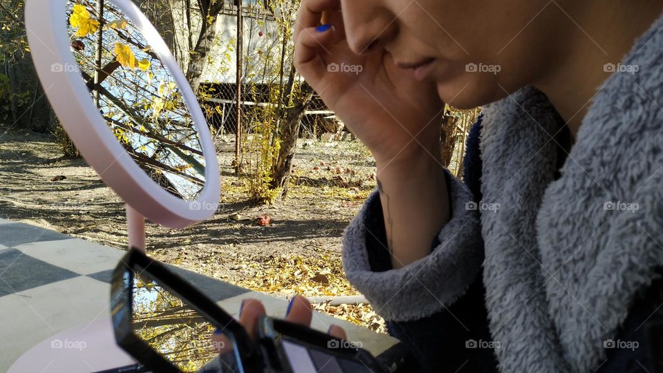 Woman doing makeup in nature in sunny autumn weather