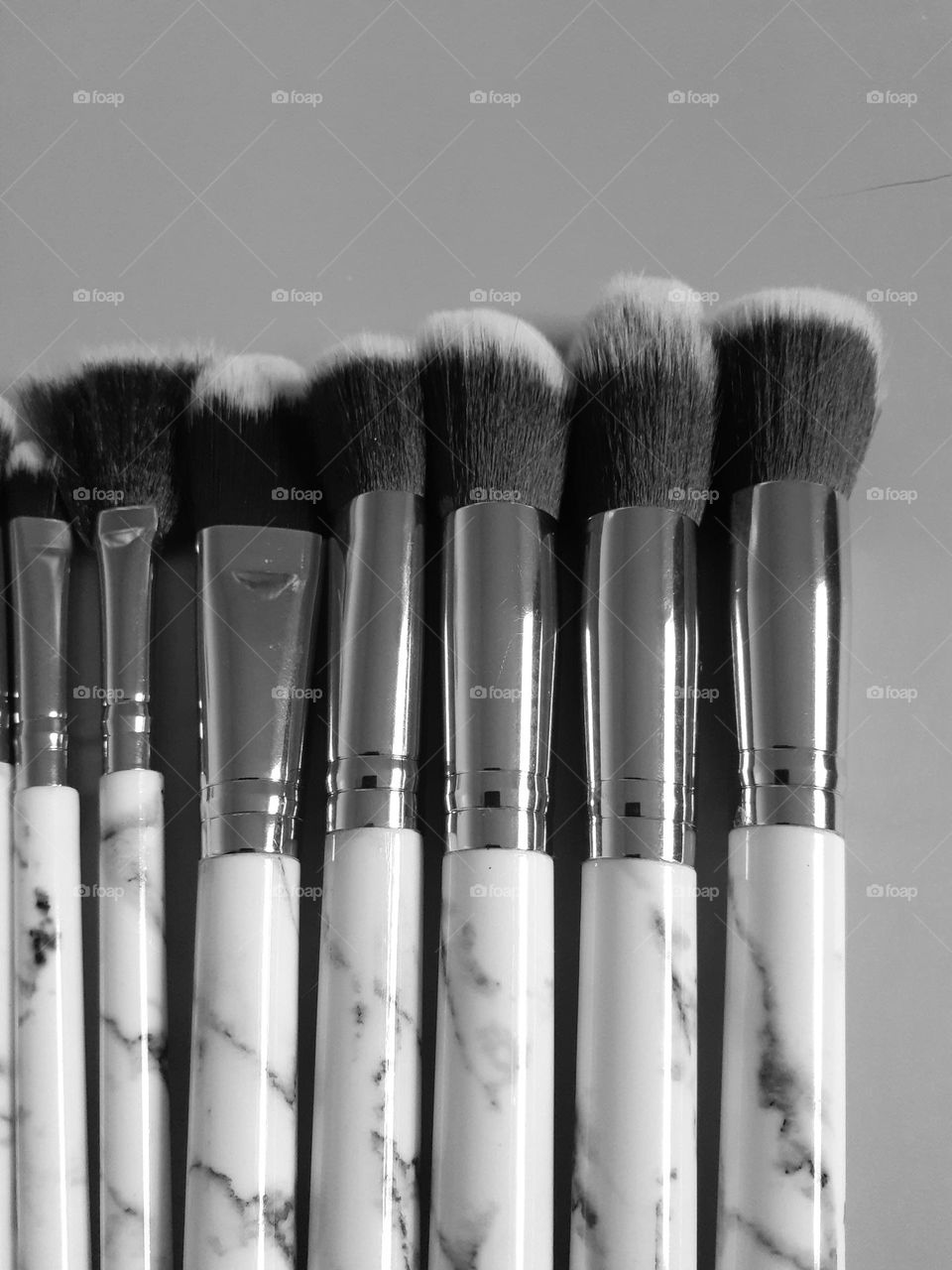 A black and white photo of makeup brushes in varying sizes lined up from smallest to biggest.