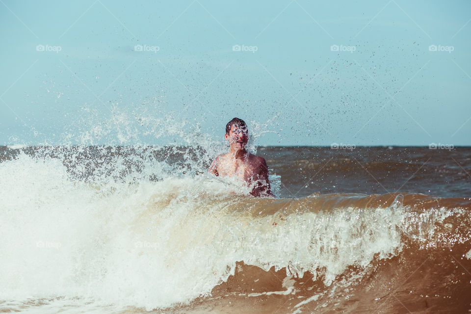 Young man enjoying the high waves in the sea during a summer vacations. Spending a summer holiday by the sea