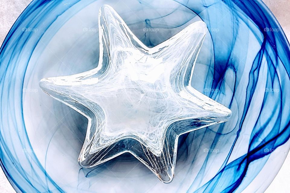 fresh and bright high key close up picture from a clear and white glass star on a blue and white swirl underground