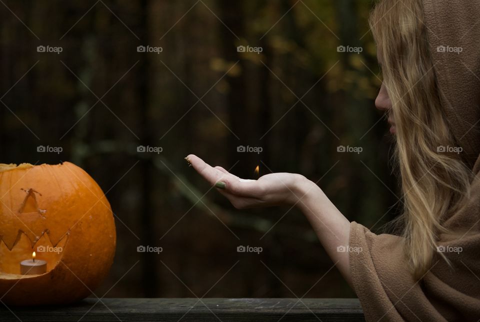 Flame of Life; Autumn setting with woman safely handling flame towards a lit pumpkin. 