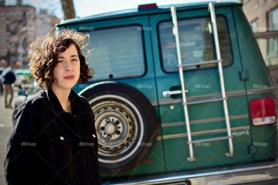 Unhappy millennial hipster in front of Chevy van askew on the curb in Manhattan.