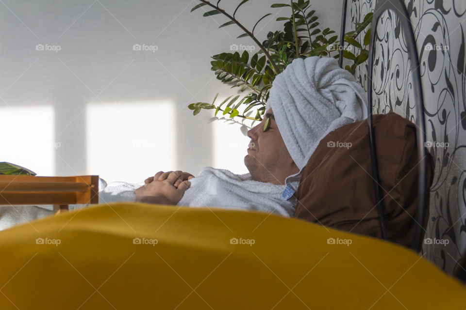 A man and home spa care at home takes care of himself and smears his face with cream, does a manicure at home on a blue background and with oranges and rests.