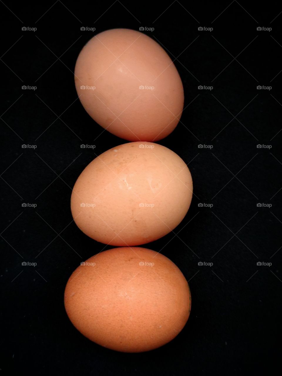 Three chicken eggs of brown color with different shades.  Black background