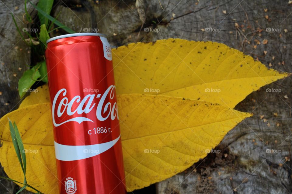 coca cola and yellow leaves on a wooden background top view