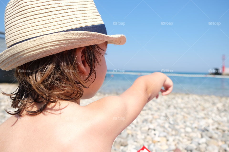 Summer at the beach. Little boy looking at the lighthouse on the sea