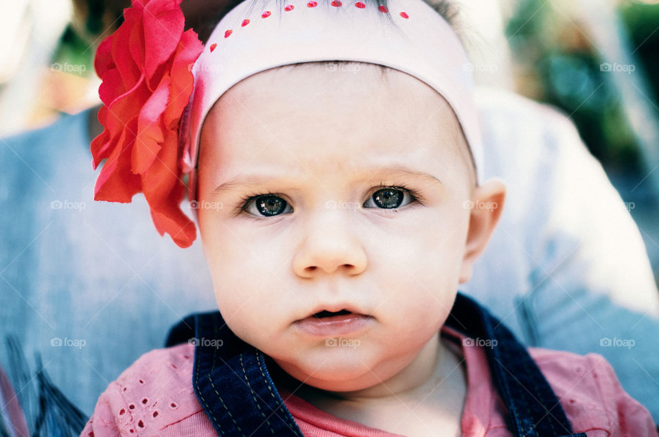 The Floret. Little baby with red flower seriously looks at the viewer.