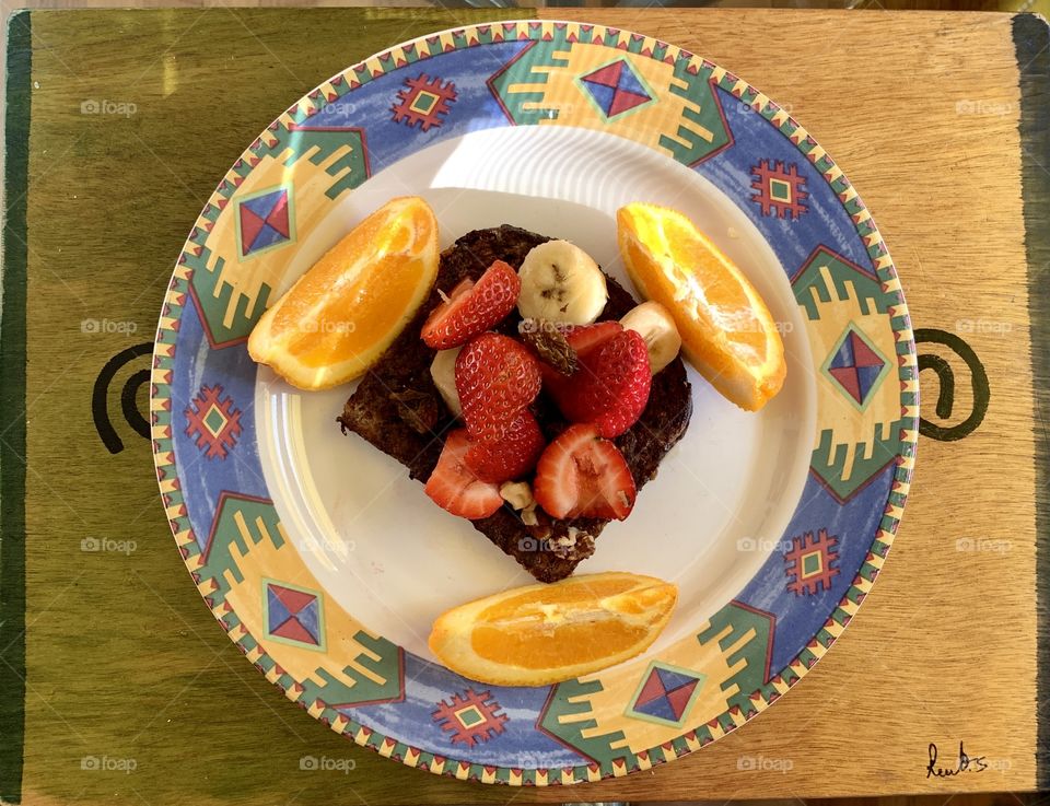 Breakfast french toasts with strawberries, bananas, walnuts, syrup. With designer plate, three slices of orange with wood place mat.