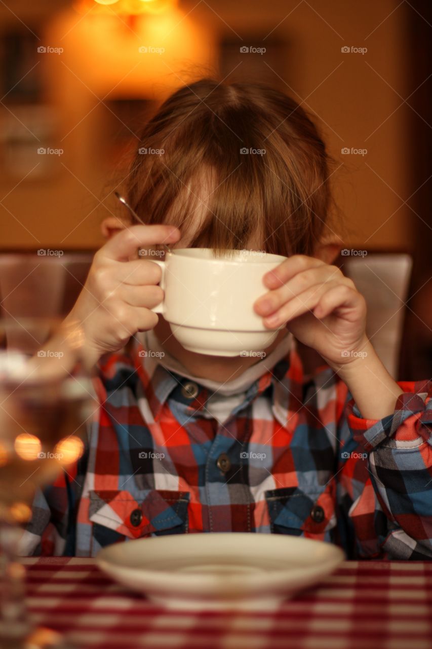 The girl at the table holds a cup of tea in her hands in front of herself