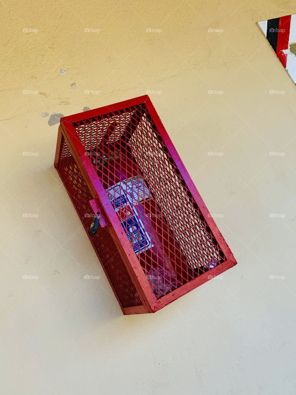 A red metal locked box with a red bottle of fire extinguisher. Fire hydrant on the wall sign of safety and security. In a messed wire and metal locker box to prevent it from theft.