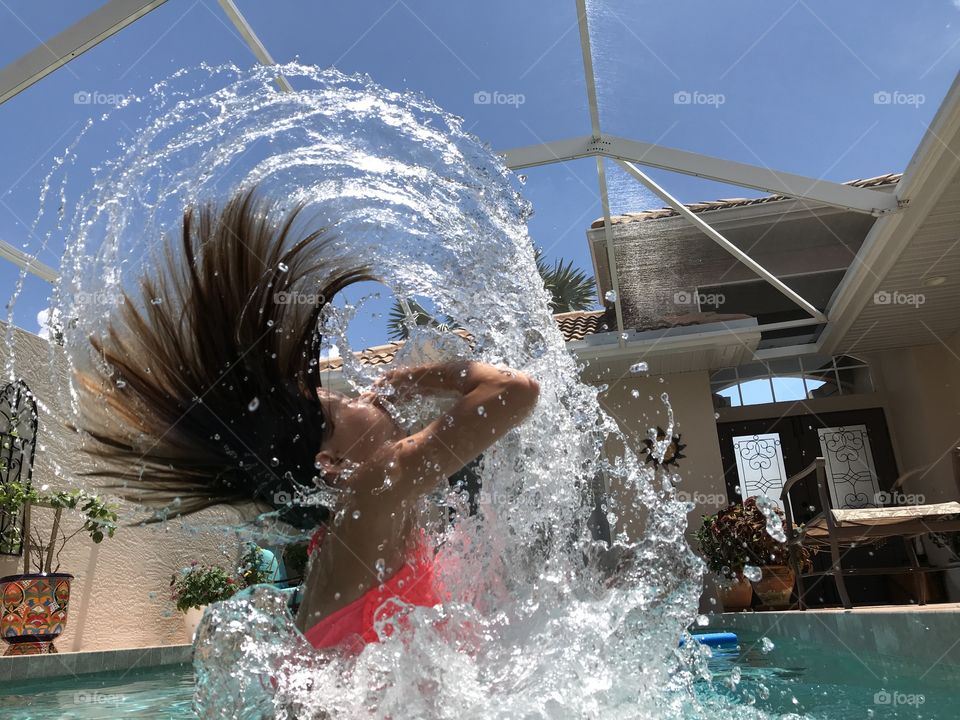 Dramatic water level picture of kid jumping out of the pool flipping her hair and water creating a Mohawk style wave. 