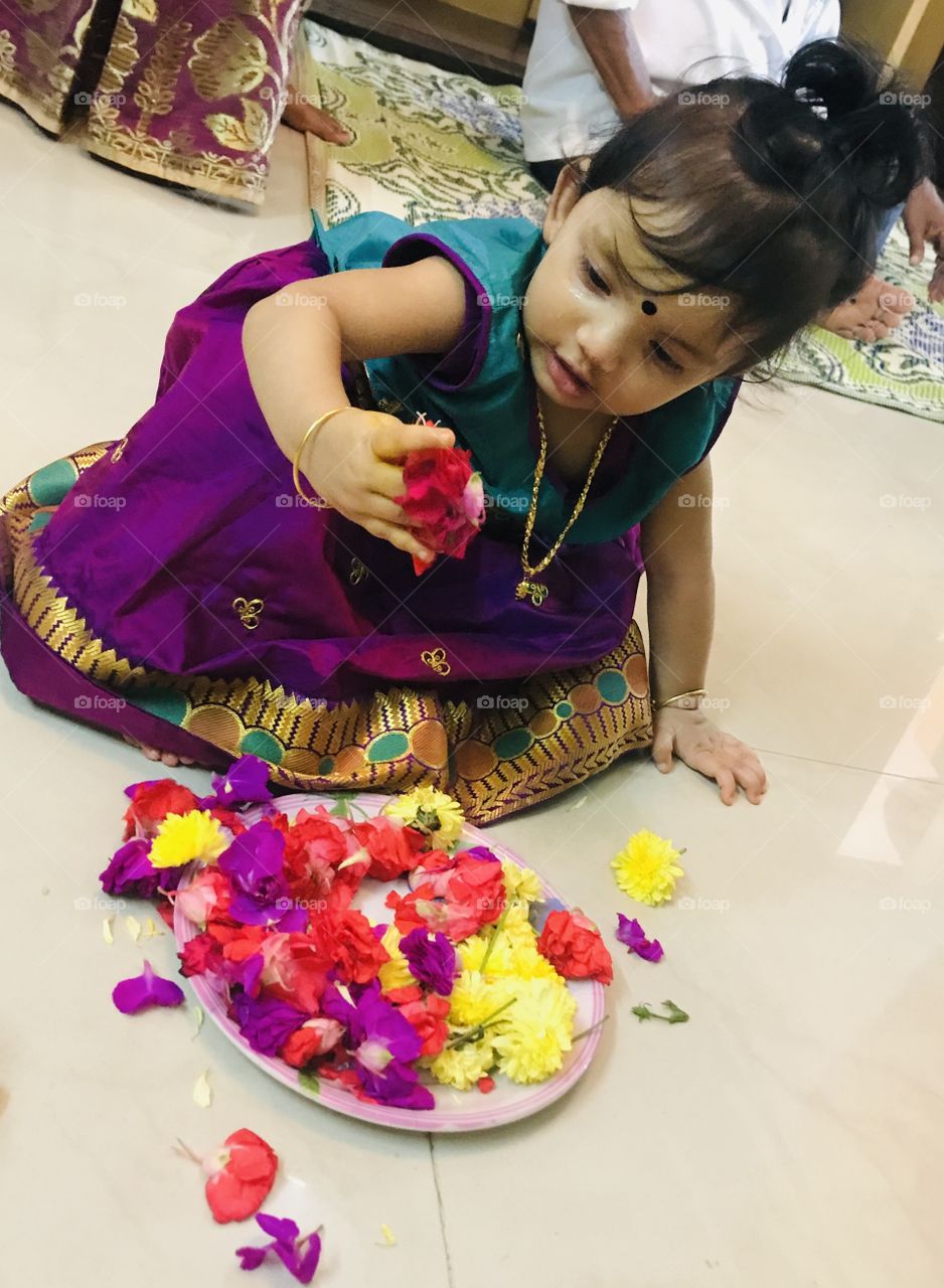 Indian little baby girl playing with multi colour flowers and wearing traditional dress 