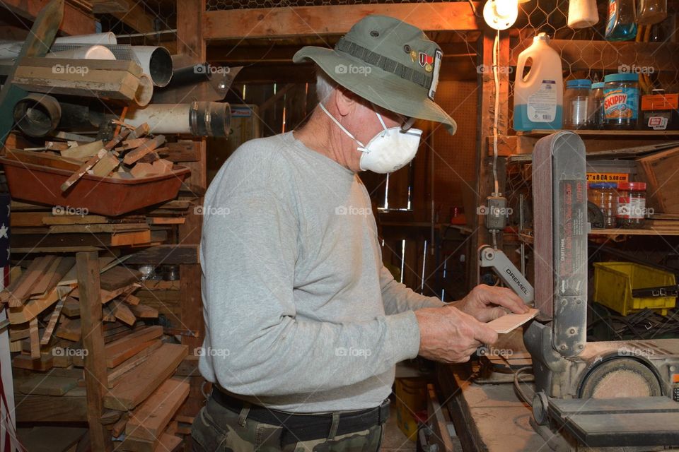 An unrecognizable man is seen in a workshop using an electric bandsaw on a small piece of wood.