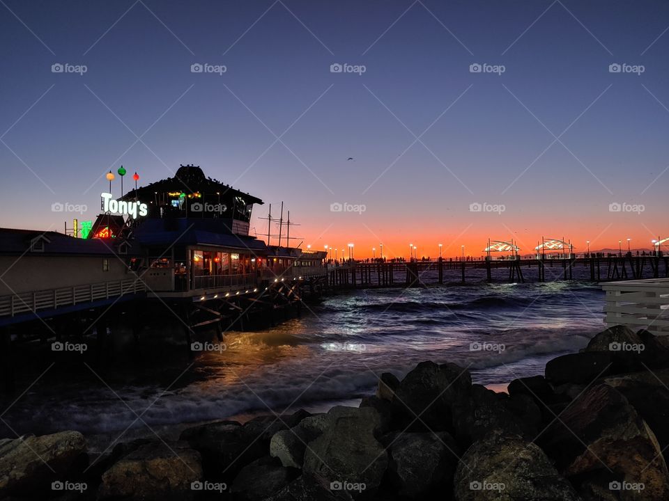 Photo shows sunset at Redondo Beach Pier with a nice transition of blue to orange skies accross the boardwalk and the beach