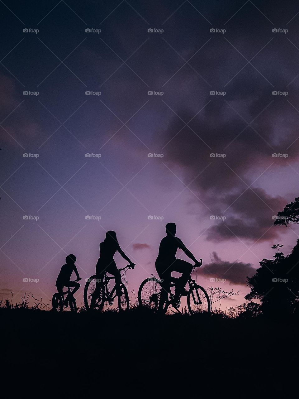 Silhouette of brothers on bicycles in front of a beautiful purple sunset