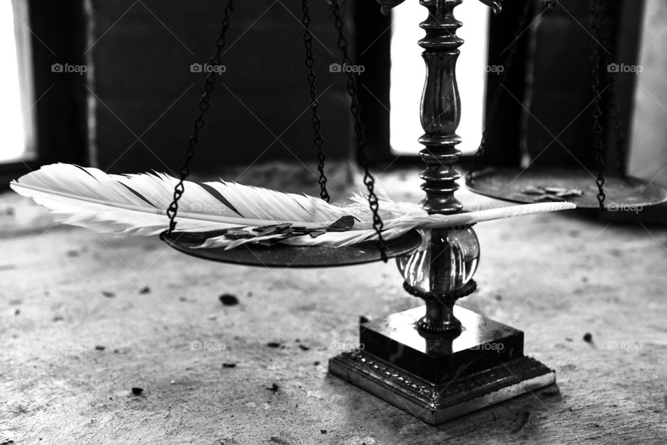 Black and white close-up of a vintage antique balance scale with a feather and small stones resting on it