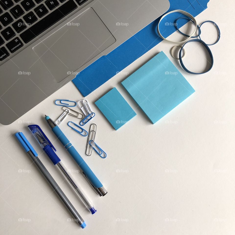 A blue themed office flay lay with a laptop and office supplies and white space