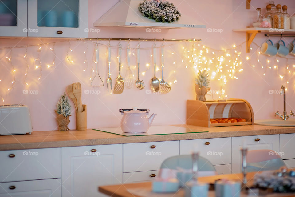 Festive winter cozy kitchen interior with garlands, decorations and gifts.  Christmas dinner at the decorated table.