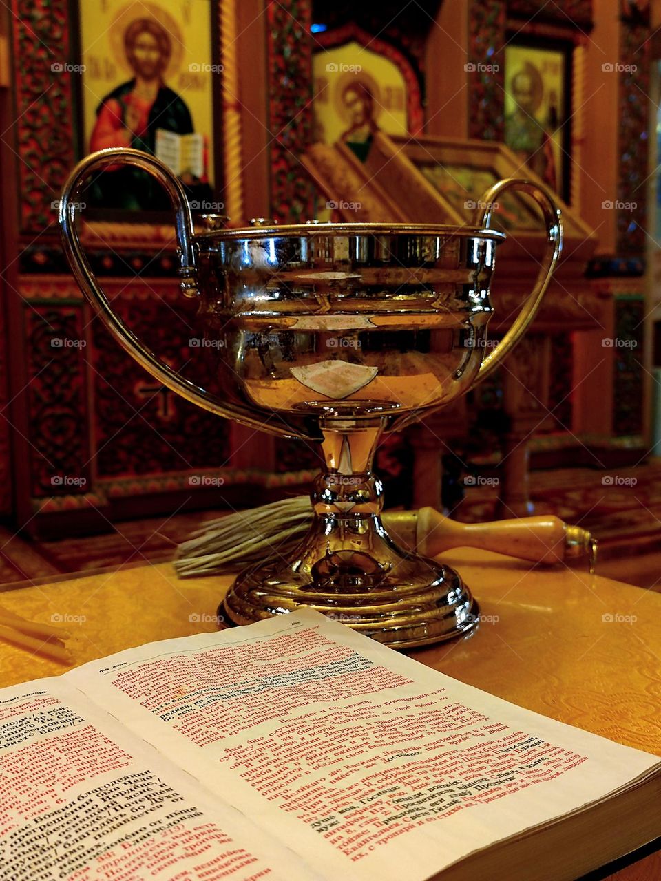 Minimalism of objects that are connected by one meaning. Church. On the stand is an open Bible, a bowl of holy water and a sprinkler. Objects on the background of icons