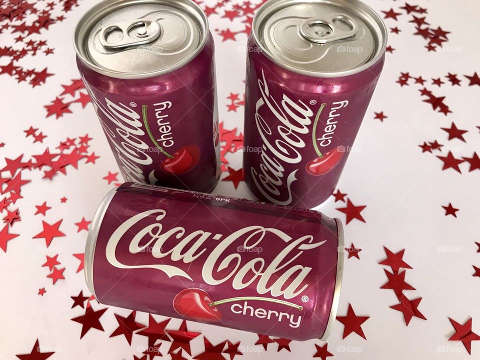 Three cans of Cherry Coca-Cola on a white background with red stars