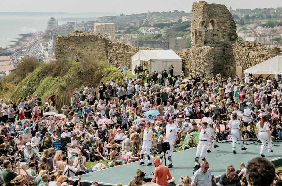 A large crowd watch Morris Dancers on a stage within the castle walls of the seaside town of Hastings, UK