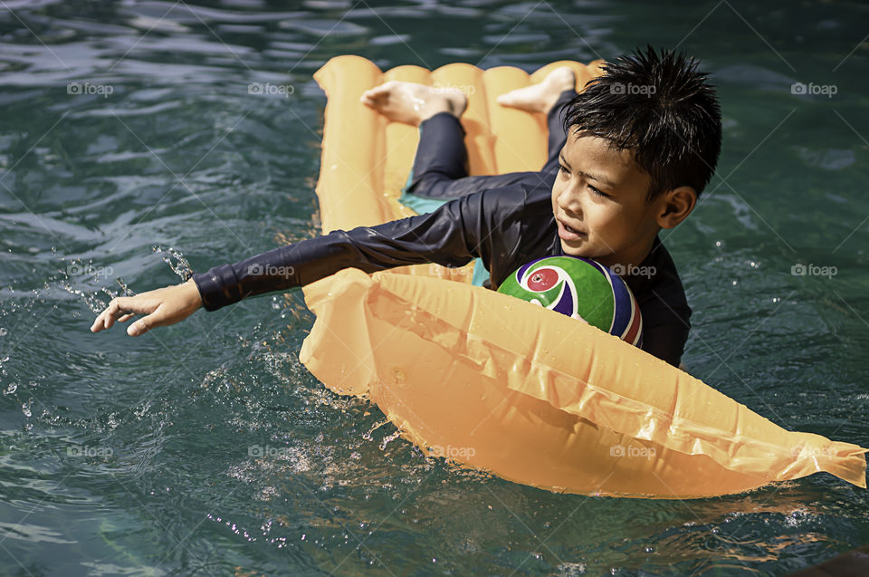 Asia boy holding the ball on the protrude in a swimming pool.