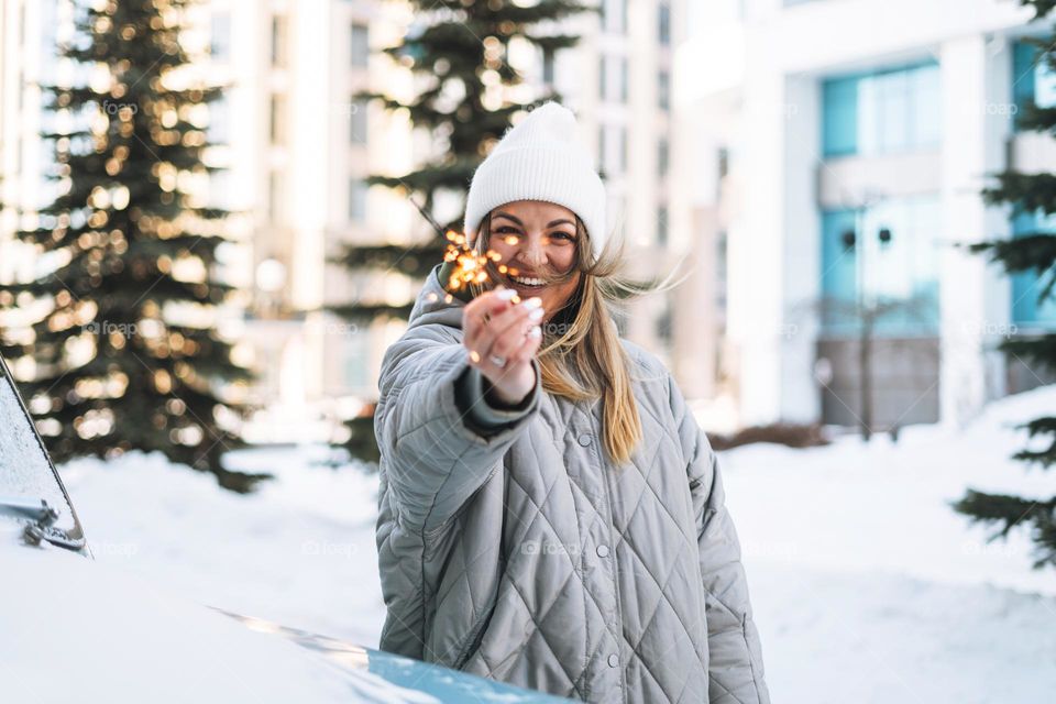 Blurred photo of Young happy woman blonde girl in warm clothes with sparkler in hands near decorated retro car in winter street