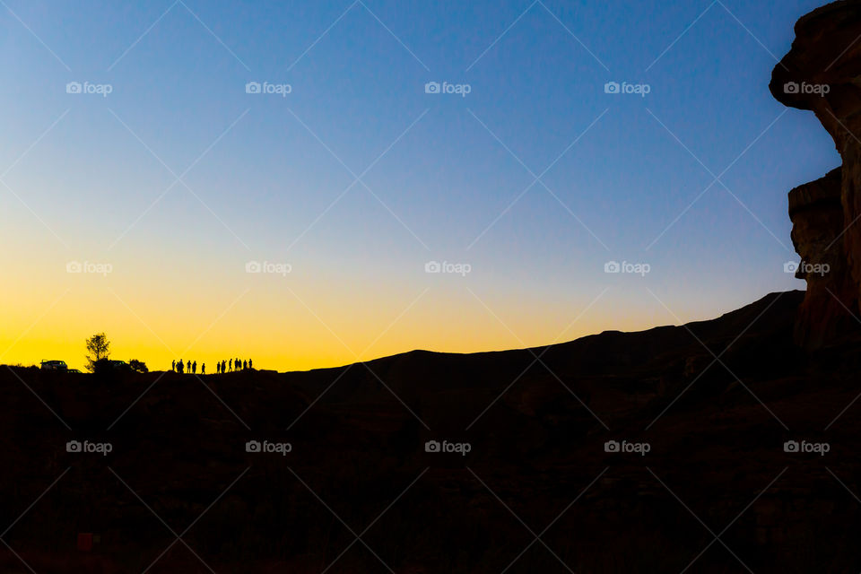 Orange and blue perfect in nature - image of sunset with group of friends against the horizon and mountains to the side.