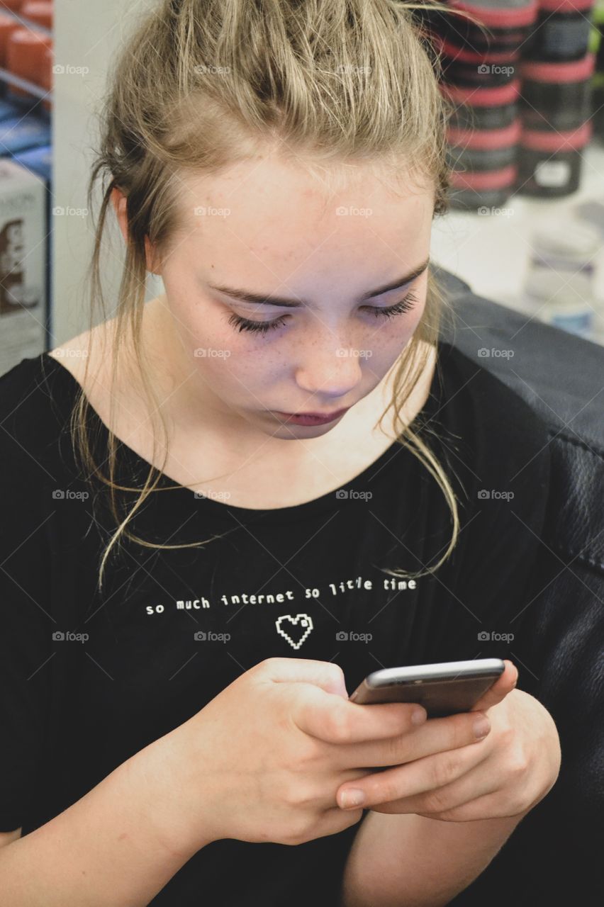 Girl using her phone, wearing a top with the text ”so much internet so little time”