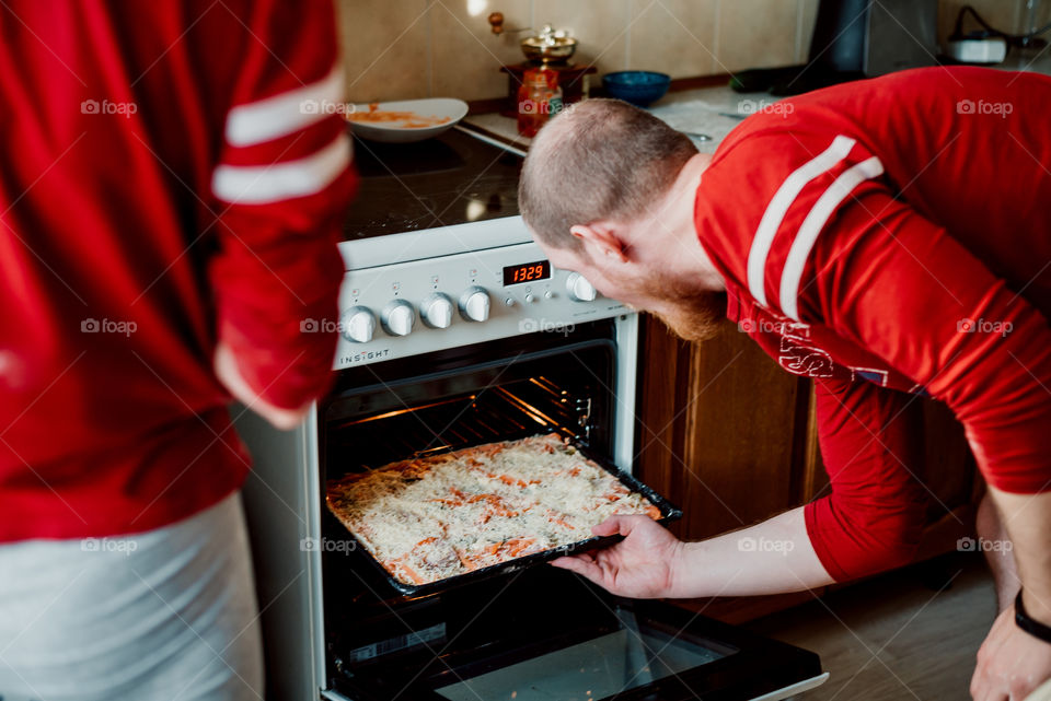 Cooking pizza with cheese at home. A man with a beard sends pizza into the oven