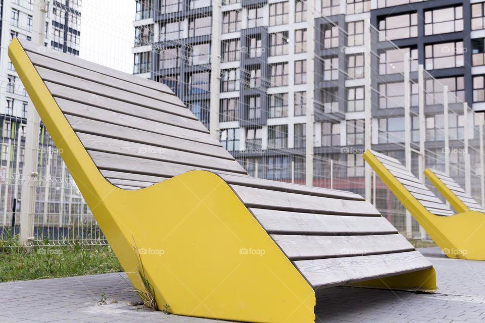 A modern, wooden bench with yellow edges in a metropolitan area.  A corner of peace and tranquility.