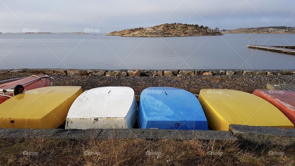 Small boats in different colors lying upside down on the shore by the sea - små båtar optimistjolle i olika färger ligger upp och ner på stranden vid havet
