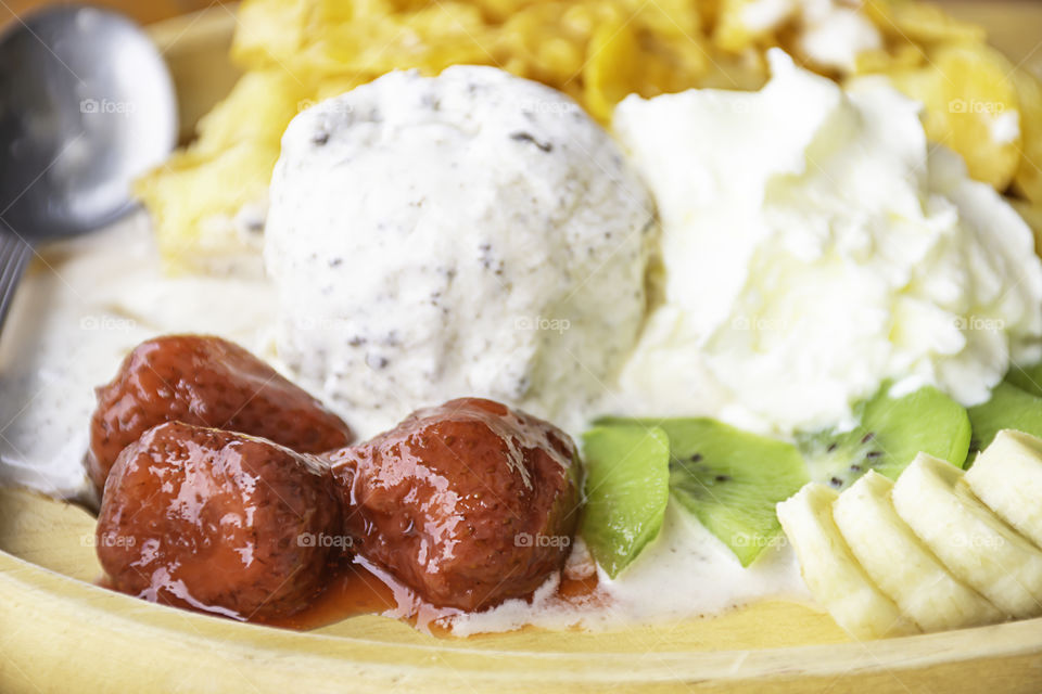 Sweet water pour on  fruits including bananas, kiwi and strawberries  with ice cream in wooden plate on table.