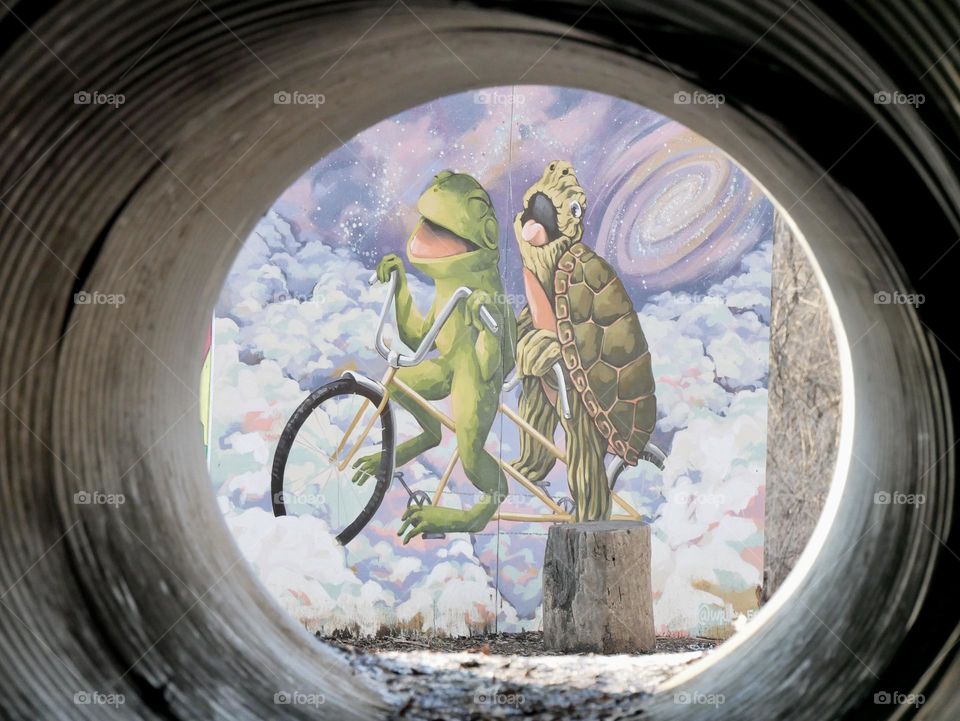 A look through a tunnel on the playground, gives a view of a full illustration of Frog and Turtle. 