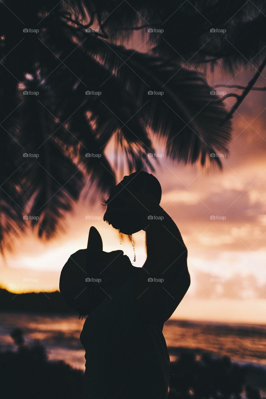 Silhouetted man drinks from coconut on tropical island.