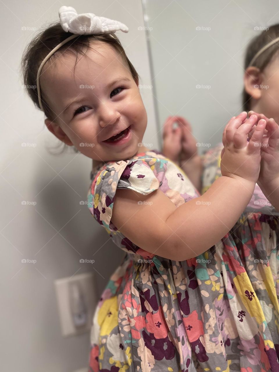 A baby girl smiling, joyful at seeing her reflection . Cute, colorful dress . Giggles!