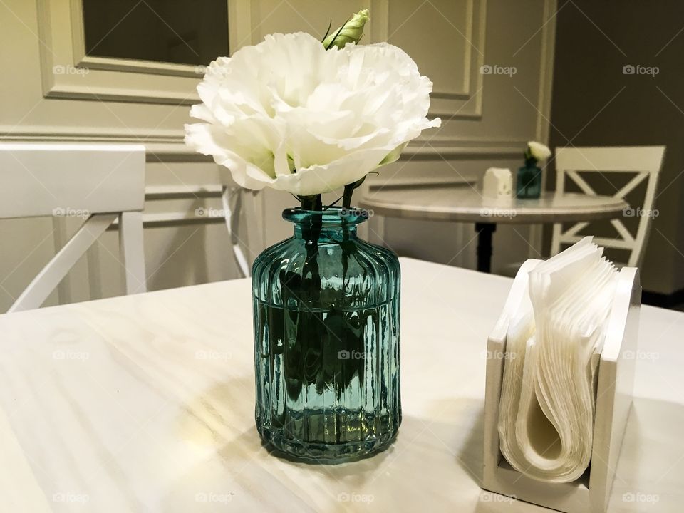 The small blue vase with white flower on the table. Floral decor at the cafe. Interior picture. 