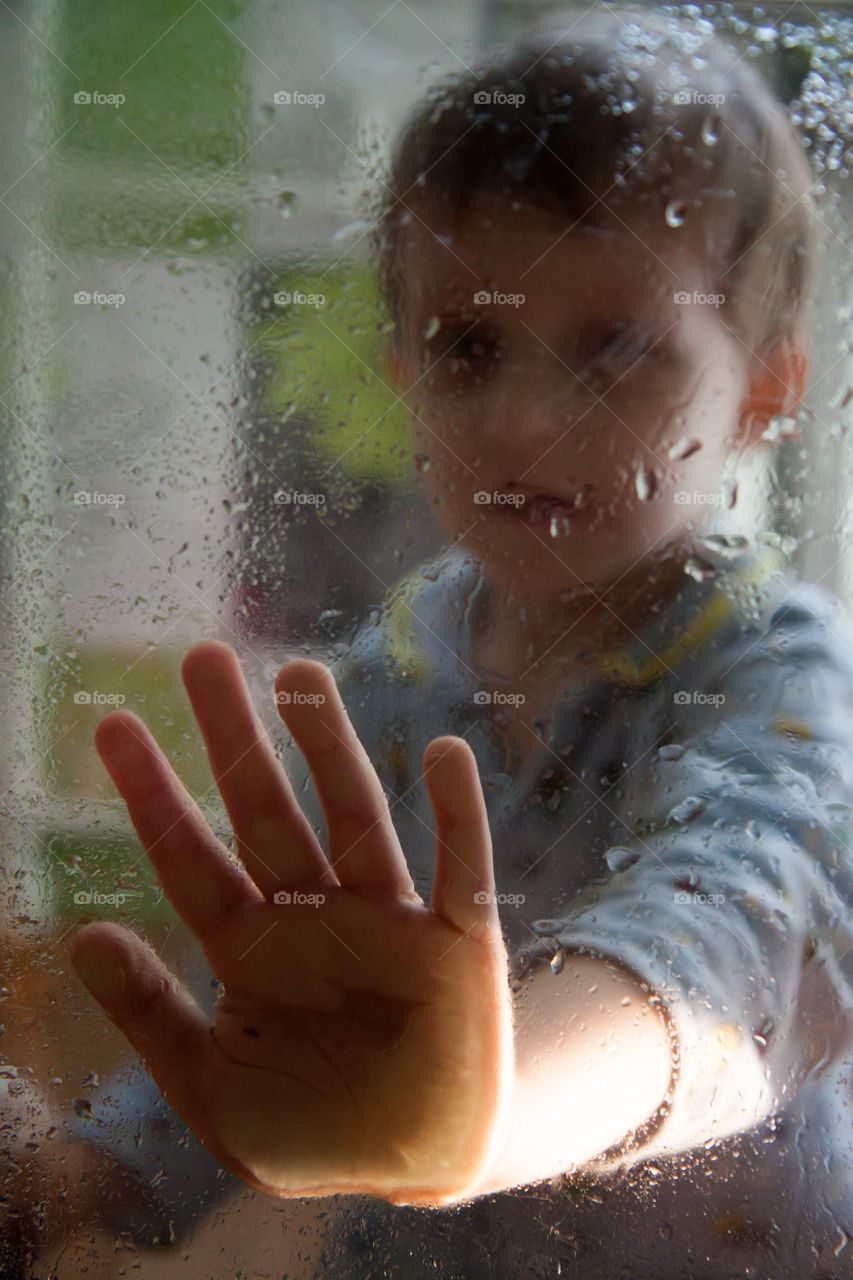 sad portrait of a boy through wet glass