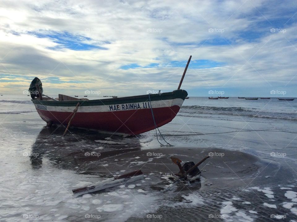 A fishing boat anchored at the beach while other boats have been raised by the tide that is slowly rising. 