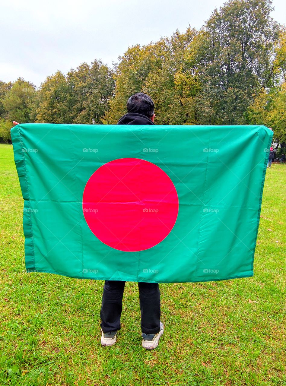 A man holds the flag of Bangladesh.  Red circle on green field