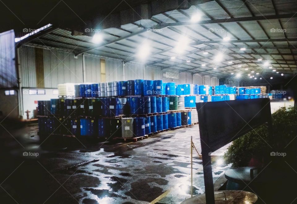 Many drums filled with liquid raw materials line up in a factory at night after rain